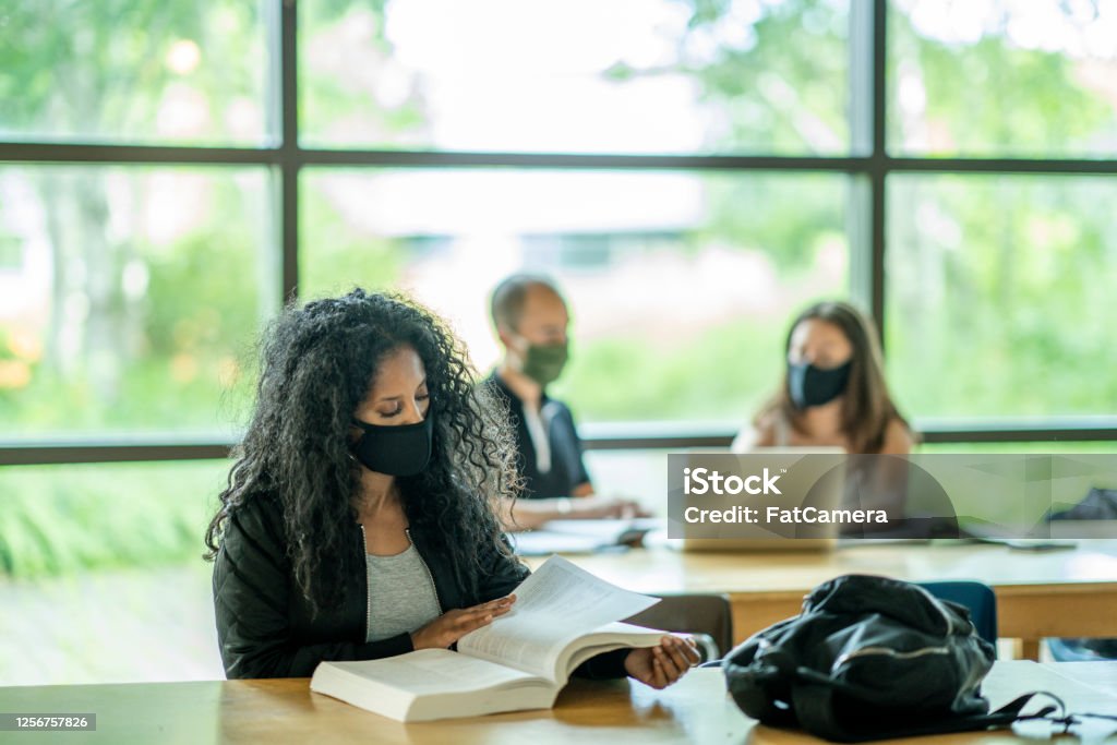 Small group of mixed ethnicity students wearing masks in a classroom Small group of college students sitting in a classroom wearing protective face masks to avoid the transfer of germs. Campus Stock Photo