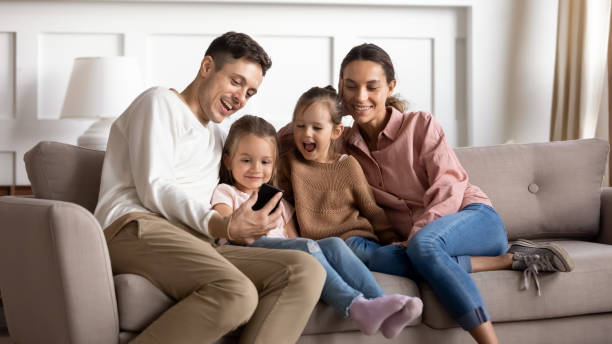 istock Happy parents with two little daughters using phone together 1256762318