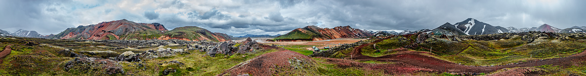 Panoramic view of colorful volcanic Landmannalaugar mountains, camping site and trail path at dramatic sky in Iceland