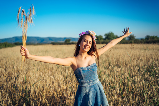Young cheerful woman standing in wheat field and holding wheat crop in her hand