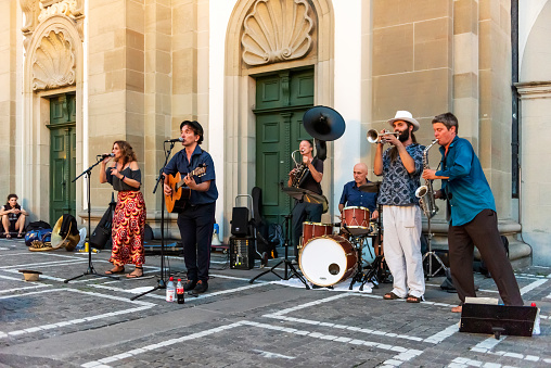 Lucerne, Switzerland - August 21, 2018: The bare brass band busking at Lucerne, Switzerland. Young boys and girls are earning money by using classic musical instruments (trombone, saxophone, oboe, drums, guitar, and soloist) in street of Geneva. They are street musicians.