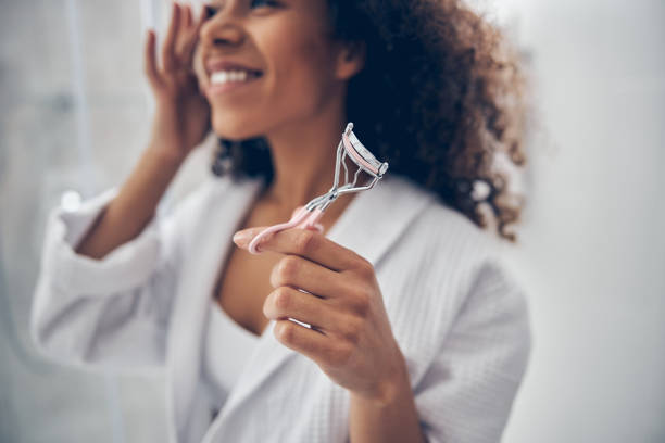 化粧品のツールを示す笑顔の陽気な女性 - lash curler ストックフォトと画像