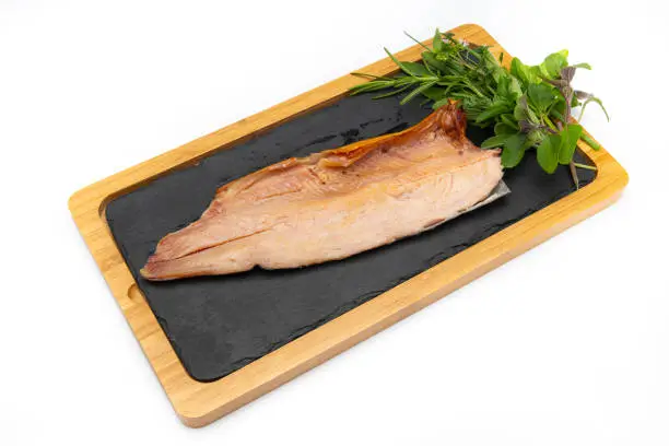Image of a smoked rainbow trout over a bamboo and black stone tray with rosemary and basil