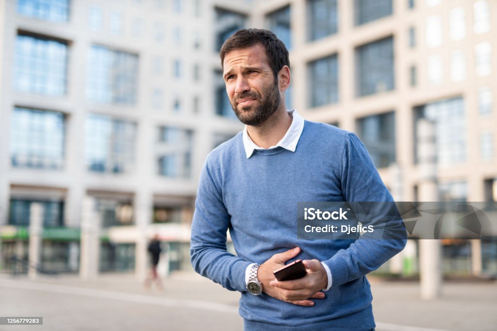 Man in the city having stomachache. Casual Mid adult man having stomach pain while walking in the city. Stomachache Stock Photo