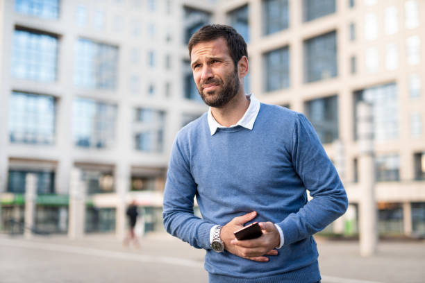 Man in the city having stomachache. Casual Mid adult man having stomach pain while walking in the city. uncomfortable stock pictures, royalty-free photos & images