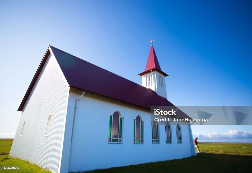 Vik, Iceland: Man at Sunlit Church (Reyniskirkja), Blue Sky Vik, Iceland: Man at Red and White Sunlit Church (Reyniskirkja), Blue Sky Background. Adult Stock Photo