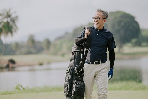 side view of a matured man golfer carrying a golf bag looking away in the golf course