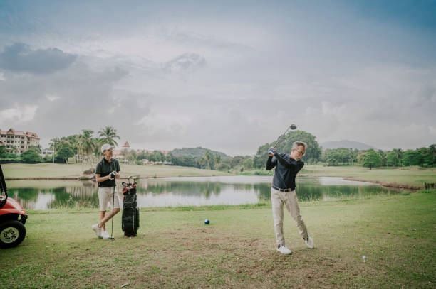 un ragazzo maturo cinese asiatico tee off swing il suo club driver al tee off point campo da golf nel fine settimana, mentre suo figlio a guardare - golf playing teeing off men foto e immagini stock