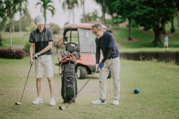 un adulto maduro chino asiático seleccionando el club de golf del conductor de la bolsa de golf para el tee off y guiando enseñando a su hijo en el campo de golf tee off point - golf expertise professional sport men fotografías e imágenes de stock