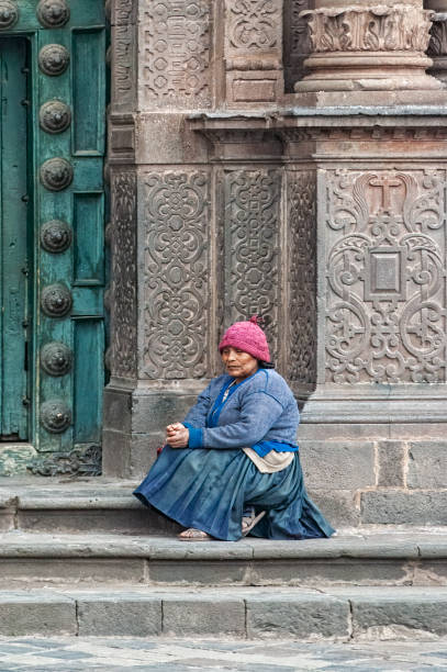 donna in abiti tradizionali seduta di fronte alla cattedrale delle ornate porte verdi in legno della cattedrale di santo domingo a cusco, in perù. - cothing foto e immagini stock
