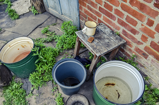 Buckets and large pans of water stand outside near a red brick wall - top view. Empty dishes in the yard of a rural house in Sumy region (Ukraine)