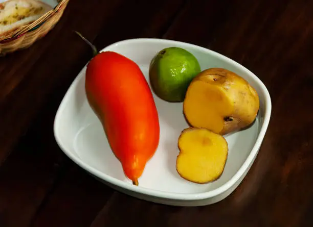 Photo of Typical foods and ingredients of Peru. Yellow potato (papa amarilla),  a highly popular potato, orange pepper (aji amarillo), and lime on a dark wooden tabletop.