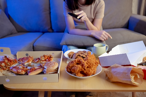 Joven asiática mujer para llevar comer comida chatarra poco saludable en el sofá viendo la serie de televisión comer comida rápida y beber en la sala de estar disfrutar de la felicidad en casa. photo