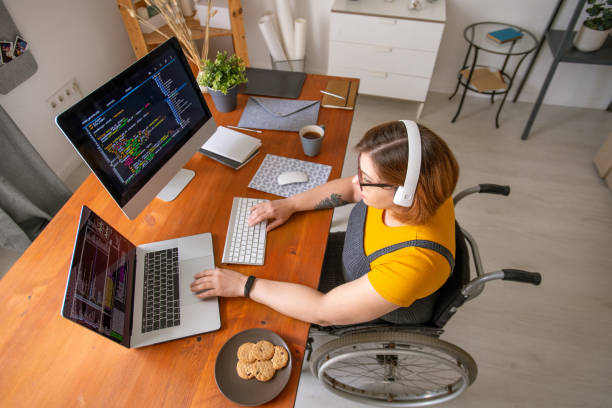 istock Young female programmer in wheelchair looking at data on laptop display 1256819037