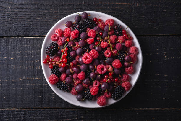 tasty fresh ripe raspberry, blackberry, gooseberry and red currant berries in plate, healthy food fruit on dark wooden background, top view - berry fruit currant variation gooseberry imagens e fotografias de stock