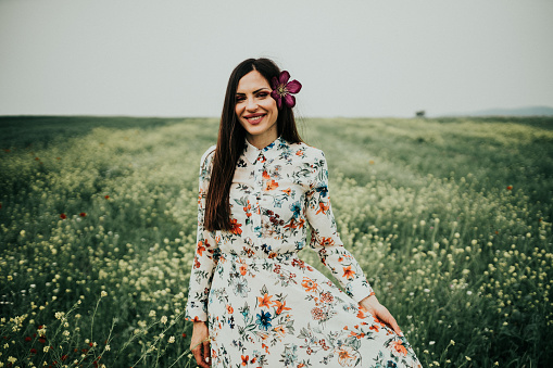 Young woman wearing fashionable dress enjoying a beautiful sunny summer day in the flower field