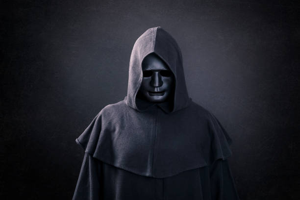 figura spaventosa con maschera in mantello incappucciato al buio - uomo incappucciato foto e immagini stock