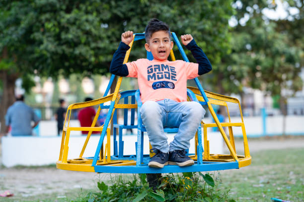 Cute little kid playing in playground. He is sitting on a roundabout and enjoying his ride.