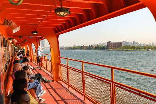 New York City, USA - August 2010: People sittting outside on the deck of a Staten Island ferry in New York City as it sails past Governor's Island.