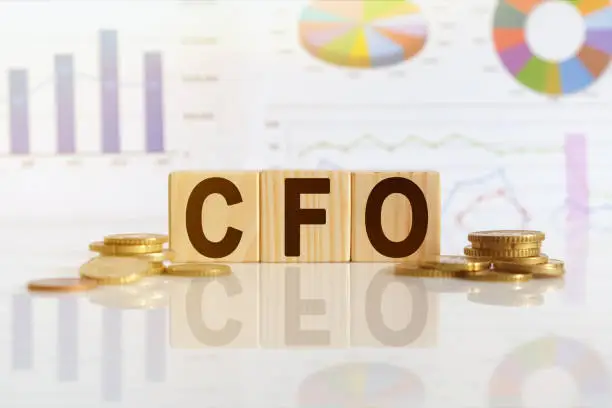 Photo of CFO the word on wooden cubes, cubes stand on a reflective surface, in the background is a business diagram.