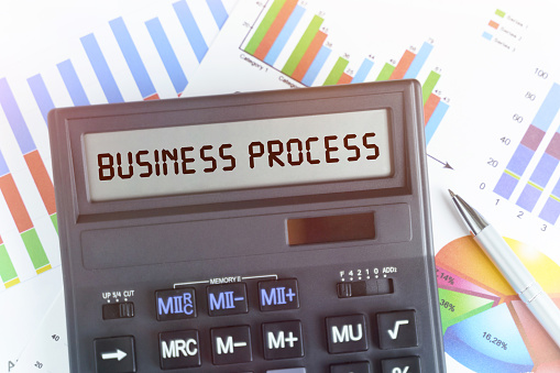 The concept of business and finance. On the table are financial charts and a calculator, on the electronic board of which is written the text - BUSINESS PROCESS