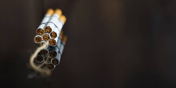 сигареты скручиваются в динамитную шашку с нитью на черной отражающей поверхности. - dynamite smoking cigarette cancer стоковые фото и изображения