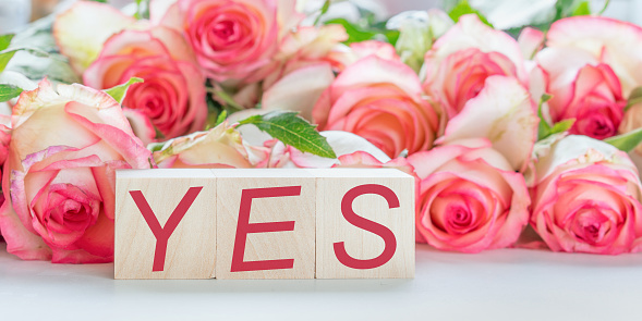 sign and text yes written on wooden blocks love and wedding concept bouquet of red roses flowers background