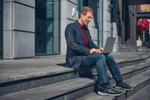 istock Good-looking stylish man using laptop on the street 1256842897