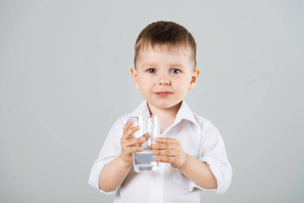 istock Little boy drinking water from glass on gray background 1256845768