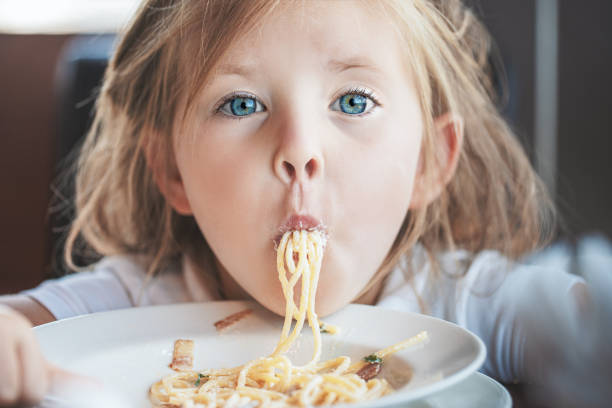 テーブルでスパゲッティを食べる愛らしい小さな女の子 - child eating pasta spaghetti ストックフォトと画像