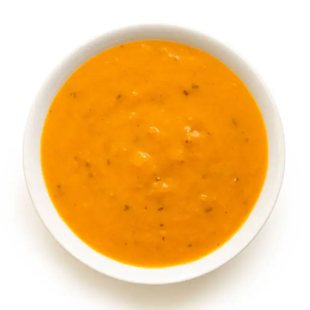 Carrot and coriander soup in a white ceramic bowl isolated on white. Top view.