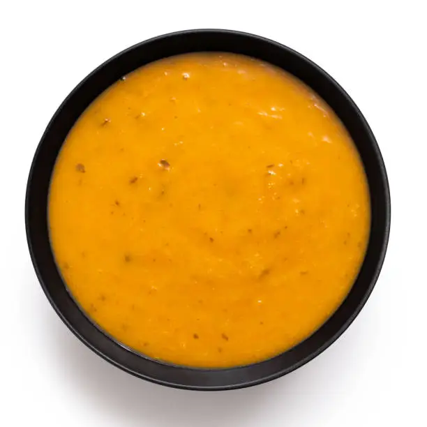 Carrot and coriander soup in a black ceramic bowl isolated on white. Top view.