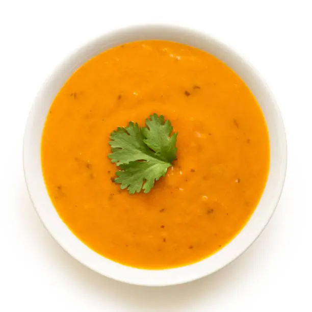 Carrot and coriander soup with fresh coriander garnish in a white ceramic bowl isolated on white. Top view.