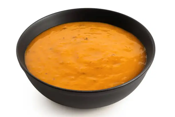 Carrot and coriander soup in a black ceramic bowl isolated on white. High angle.
