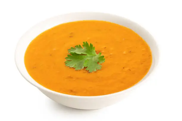 Carrot and coriander soup with fresh coriander garnish in a white ceramic bowl isolated on white. High angle.