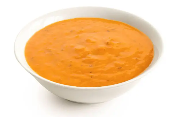 Carrot and coriander soup in a white ceramic bowl isolated on white. High angle.