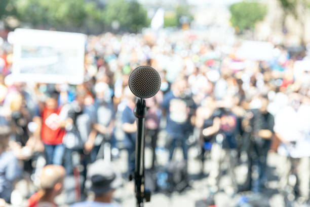 istock Focus on microphone, blurred group of people at protest in the background 1256851338