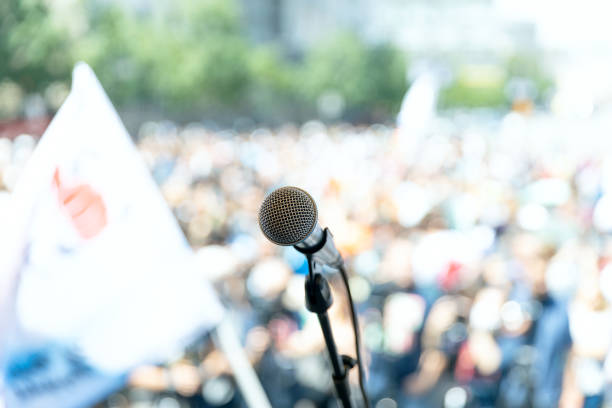 istock Focus on microphone, blurred group of people at protest in the background 1256852691