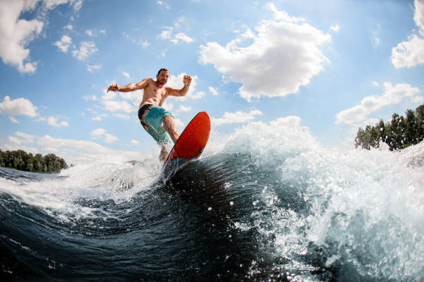 giovane uomo attraente bilanciamento su tavola da surf sull'onda del fiume creato da barca - wakeboarding surfing men vacations foto e immagini stock