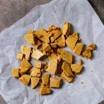 Homemade honeycomb hokey pokey or cinder toffee or dalgona korean sugar candies on baking paper over grey concrete background. Flat lay, space
