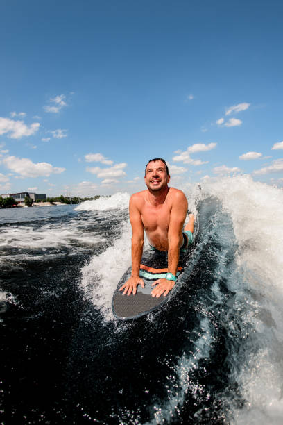 istock Adult smiling man rides wave while lying on surfboard. 1256859981