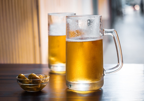 Two mugs of light beer with a snack without people. Unbottled fresh cold beer on the table in the open-air street pub in a soft sun light.