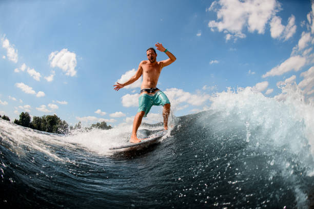 istock cheerful athletic guy actively ride on the waves on surfboard against blue sky 1256861350