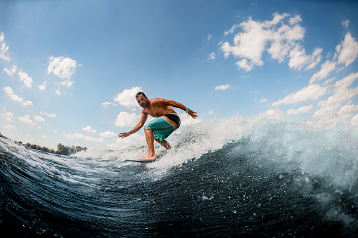 young athletic guy wakesurfer actively ride on the waves on a surfboard against a blue sky