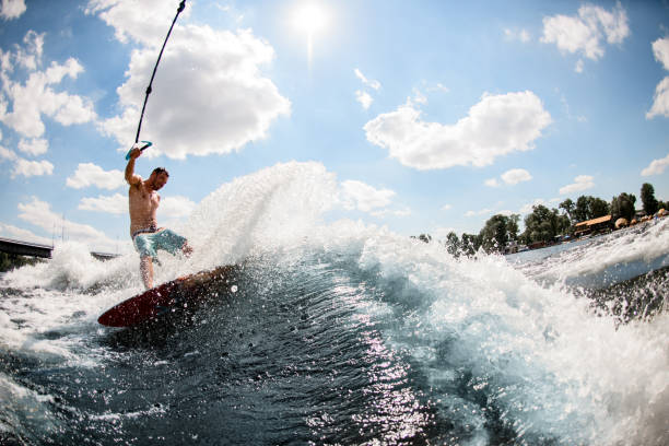 adulto bell'uomo wakesurfing sul fiume e tirato da una barca. - wakeboarding surfing men vacations foto e immagini stock