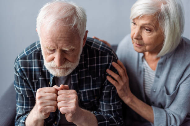 besorgte seniorin berührt mann, der an demenz leidet und mit geballten fäusten sitzt - senior adult depression dementia alzheimers disease stock-fotos und bilder