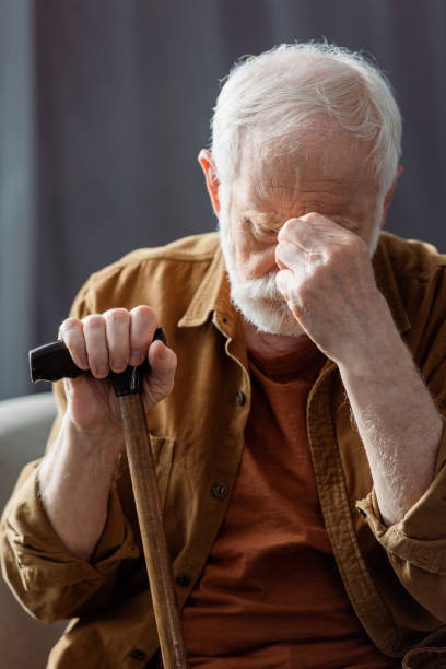istock senior, lonely man touching face while sitting with walking stick 1256862840