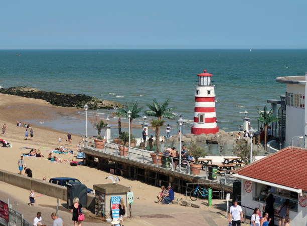 Beach and café with lighthouse next to pier at Clacton in Essex Beach at Clacton next to the Pier with a café and model red and white striped lighthouse. Tourists outdoors on a Sunny summers day. Clacton on Sea, Essex, United Kingdom, July 17, 2020 clacton on sea stock pictures, royalty-free photos & images