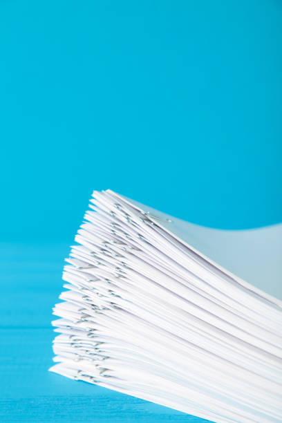 Stack of white paper with clips on blue background. Top view
