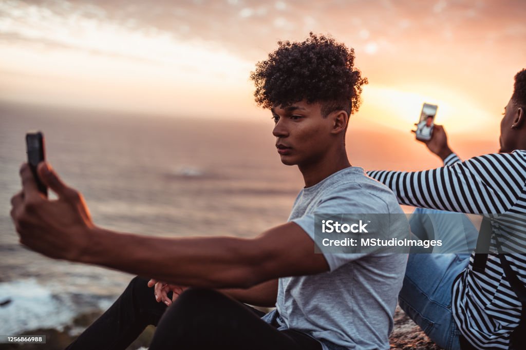 Two young men taking selfies from different angles Two young men sitting and taking a selfies Communication Stock Photo